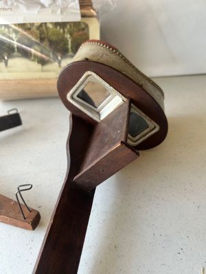 Sale Photo Thumbnail #158: An antique hand-held stereoscope viewer featuring an embossed metal hood with ornate floral and crest details stamped 'MONARCH', a wooden body, folding handle, glass lenses, and slide track. Accompanied by a stack of vintage stereoview/stereograph cards s