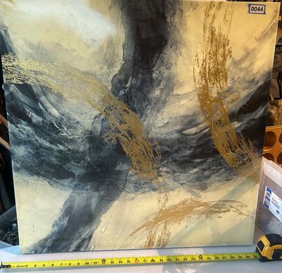 Sale Photo Thumbnail #44: A large contemporary square canvas wall art featuring dynamic fluid abstract brushstrokes in shades of charcoal, gray, and cream, highlighted with textured gold metallic/foil sweeping accents. Includes a measuring tape in the photo showing a width of appr