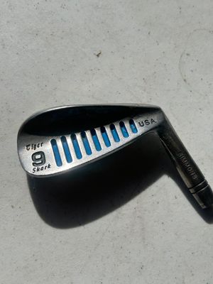 Sale Photo Thumbnail #112: A collection of vintage golf iron club heads including Simmons Tiger Shark USA models (3-iron, 8-iron, 9-iron, and others). Metal construction with signature blue cavity slot fill and etched shark logo details. Heads show play wear and surface patina typi