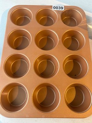 Sale Photo Thumbnail #39: A copper-toned non-stick metal baking pan featuring 12 standard-sized muffin or cupcake cups. Appears in good, gently used condition with minor surface wear from handling.