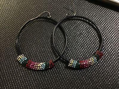 Sale Photo Thumbnail #79: Pair of thin black hoop drop earrings featuring curved bar sections set with colorful pavé rhinestones in shades of red, pink, green, blue, yellow, and clear. Fitted with silver-tone wire French ear hooks. In good pre-owned condition with all rhinestones