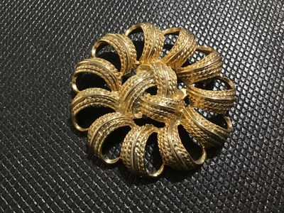 Sale Photo Thumbnail #113: A vintage gold-tone costume jewelry brooch featuring a openwork circular design with textured, looped ribbon-style petals and a knot center motif. The back features a standard rollover safety clasp mechanism. Shows light surface wear consistent with age a