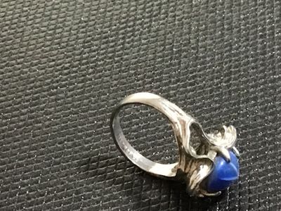 Sale Photo Thumbnail #134: Vintage statement ring featuring an oval cabochon blue star sapphire (asterism evident) set in an ornate, textured white gold mounting. Stamped '' inside the band alongside a maker's mark. Ring size measures approximately 5.5 - 5.75 on mandrel. Pre-owned 