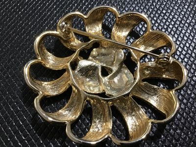 Sale Photo Thumbnail #114: A vintage gold-tone costume jewelry brooch featuring a openwork circular design with textured, looped ribbon-style petals and a knot center motif. The back features a standard rollover safety clasp mechanism. Shows light surface wear consistent with age a