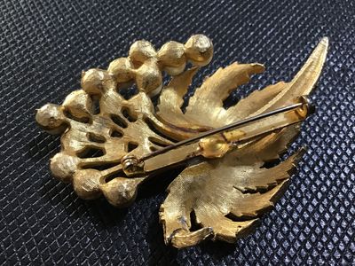 Sale Photo Thumbnail #91: A vintage mid-century style brooch featuring textured, brushed gold-tone leaves accenting a cluster of round faux pearls. Includes a standard pin-back clasp mechanism on the reverse. Shows minor age-appropriate wear and slight tarnishing on the back setti