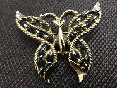 Sale Photo Thumbnail #21: A vintage gold-tone metal butterfly brooch featuring textured rope-like openwork wings accented with blue painted highlights. Includes a standard roll-over safety clasp pin mechanism on the back. Shows light surface wear consistent with age.