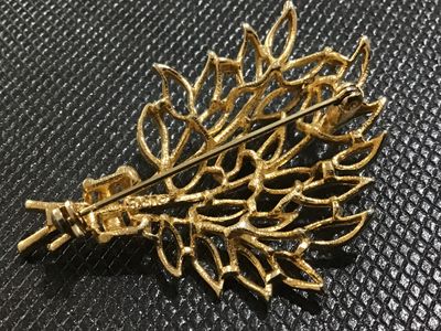Sale Photo Thumbnail #82: Vintage gold-tone brooch featuring an intricate openwork leaf spray or bouquet motif with textured and beaded detailing. Marked 'Lisner on the reverse side. Secured with a standard pin stem and rollover safety clasp. Shows light vintage wear appropriate f