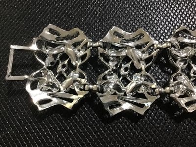 Sale Photo Thumbnail #106: A vintage silver-tone wide link bracelet featuring stylized floral textured leaf motifs within openwork geometric frames. Secured with a fold-over clasp. Appears to be mid-20th century costume jewelry in good condition with minor surface wear visible on t