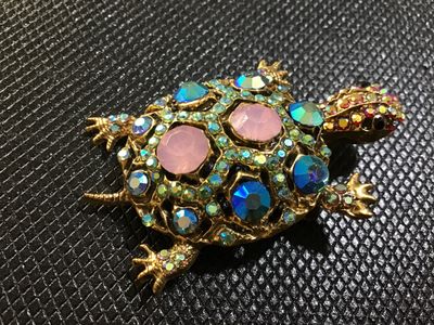 Sale Photo Thumbnail #69: Ornate gold-tone turtle brooch embellished with colorful rhinestones, including iridescent aurora borealis, blue, pink, and small accent stones. Features a filigree textured back with a standard pin stem and rollover clasp. In good vintage condition with 