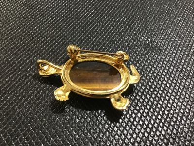 Sale Photo Thumbnail #61: Gold-tone turtle motif pin/brooch featuring a carved or etched tiger's eye cabochon shell. Includes a bail on the back so it can also be worn as a necklace pendant. Gold finish shows light surface wear/aging. Pin mechanism on back is intact and functional