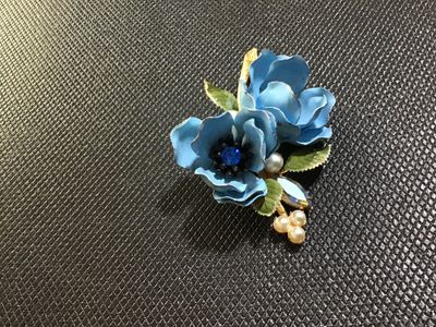 Sale Photo Thumbnail #87: A vintage Weiss gold-tone floral brooch featuring two light blue enameled flowers with blue rhinestone centers, faux pearl accents, a navette aurora borealis rhinestone, and green enamel leaves. Marked '© WEISS' on the back frame. Pin mechanism is intact