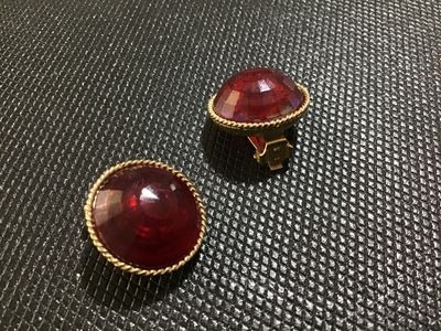 Sale Photo Thumbnail #46: Pair of vintage clip-on earrings featuring round, domed red lucite or resin cabochons set in textured gold-tone metal frames with rope-twist border detailing. Clips show slight vintage wear but are intact and fully functional. Unmarked.