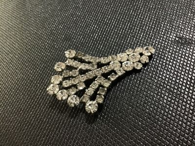 Sale Photo Thumbnail #29: Vintage silver-tone metal and clear rhinestone fan spray brooch. Features prong-set and channel-set faceted glass rhinestones arranged in a tiered, spreading fan design with a rollover safety clasp on the back. Showcases minor light surface wear and sligh