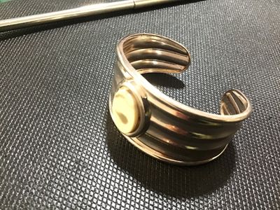 Sale Photo Thumbnail #101: Silver-tone wide ribbed cuff bracelet featuring a central bezel-set oval stone or cabochon accent in a light cream tone. Shows light surface wear and minor tarnishing consistent with pre-owned condition.