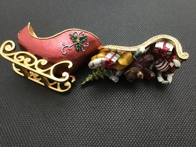 Sale Photo Thumbnail #12: Decorative enameled metal hinged trinket box shaped like a Christmas sleigh filled with toys, a teddy bear, presents, candy canes, and a Christmas tree. Features rhinestone accents along the rim, gold-tone metal runners, magnetic closure, and a painted en