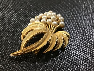 Sale Photo Thumbnail #92: A vintage mid-century style brooch featuring textured, brushed gold-tone leaves accenting a cluster of round faux pearls. Includes a standard pin-back clasp mechanism on the reverse. Shows minor age-appropriate wear and slight tarnishing on the back setti