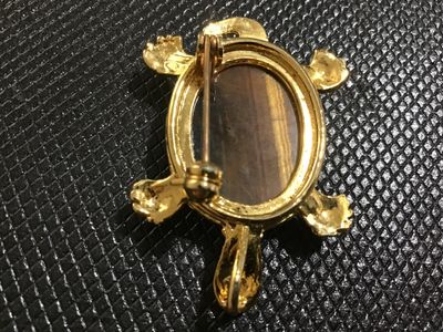 Sale Photo Thumbnail #60: Gold-tone turtle motif pin/brooch featuring a carved or etched tiger's eye cabochon shell. Includes a bail on the back so it can also be worn as a necklace pendant. Gold finish shows light surface wear/aging. Pin mechanism on back is intact and functional