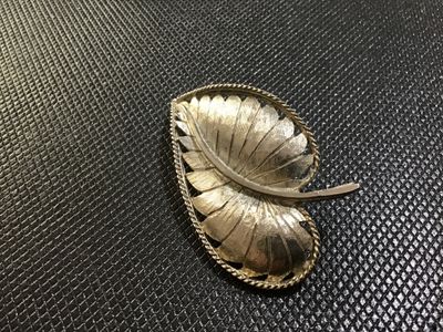 Sale Photo Thumbnail #94: A vintage gold-tone leaf brooch by BSK featuring a textured brushed metal finish, curved stem detail, and a rope twist border. The back is stamped '©BSK' and includes a standard pin stem with a rollover safety clasp. Shows light vintage wear consistent w