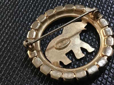 Sale Photo Thumbnail #37: A vintage gold-tone circular brooch by Napier featuring a central textured elephant motif surrounded by a halo of iridescent Aurora Borealis rhinestones. Marked 'J Warner ' on the reverse oval cartouche. Features a roll-over safety clasp. In good vintage 