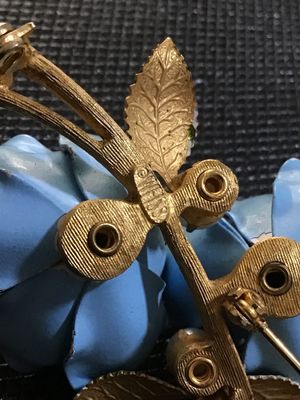 Sale Photo Thumbnail #84: A vintage Weiss gold-tone floral brooch featuring two light blue enameled flowers with blue rhinestone centers, faux pearl accents, a navette aurora borealis rhinestone, and green enamel leaves. Marked '© WEISS' on the back frame. Pin mechanism is intact