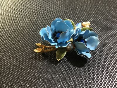 Sale Photo Thumbnail #88: A vintage Weiss gold-tone floral brooch featuring two light blue enameled flowers with blue rhinestone centers, faux pearl accents, a navette aurora borealis rhinestone, and green enamel leaves. Marked '© WEISS' on the back frame. Pin mechanism is intact