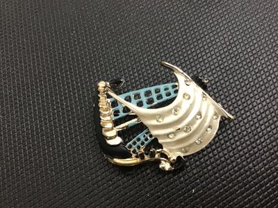 Sale Photo Thumbnail #24: Vintage nautical sailing ship brooch pin featuring white, light blue, and black enamel accents with clear rhinestone details set in gold-tone metal. Standard pin stem and safety clasp on the reverse. Shows minor wear to the enamel and finish consistent wi