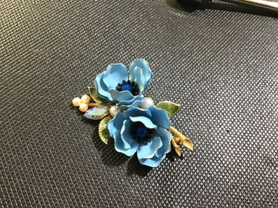 Sale Photo Thumbnail #89: A vintage Weiss gold-tone floral brooch featuring two light blue enameled flowers with blue rhinestone centers, faux pearl accents, a navette aurora borealis rhinestone, and green enamel leaves. Marked '© WEISS' on the back frame. Pin mechanism is intact