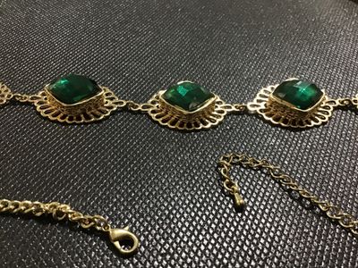 Sale Photo Thumbnail #121: Gold-tone metal statement necklace featuring three large, faceted emerald-green faux gemstone panels set in filigree frames, flanked by openwork round filigree accents. Includes an adjustable chain link with a lobster claw clasp. Appears to be in good pre