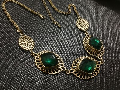 Sale Photo Thumbnail #120: Gold-tone metal statement necklace featuring three large, faceted emerald-green faux gemstone panels set in filigree frames, flanked by openwork round filigree accents. Includes an adjustable chain link with a lobster claw clasp. Appears to be in good pre