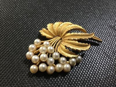 Sale Photo Thumbnail #90: A vintage mid-century style brooch featuring textured, brushed gold-tone leaves accenting a cluster of round faux pearls. Includes a standard pin-back clasp mechanism on the reverse. Shows minor age-appropriate wear and slight tarnishing on the back setti