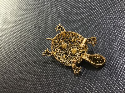 Sale Photo Thumbnail #70: Ornate gold-tone turtle brooch embellished with colorful rhinestones, including iridescent aurora borealis, blue, pink, and small accent stones. Features a filigree textured back with a standard pin stem and rollover clasp. In good vintage condition with 