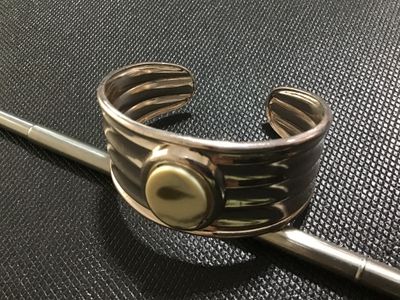 Sale Photo Thumbnail #103: Silver-tone wide ribbed cuff bracelet featuring a central bezel-set oval stone or cabochon accent in a light cream tone. Shows light surface wear and minor tarnishing consistent with pre-owned condition.