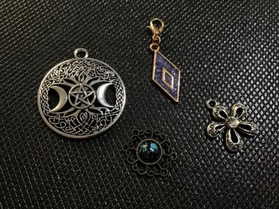 Sale Photo Thumbnail #77: A collection of 4 modern costume jewelry charms and pendants. Includes a silver-tone Celtic triple moon and pentagram pendant, a gold-tone glittery diamond-shaped charm with a lobster clasp, a silver-tone flower-shaped charm with a central crystal accent,