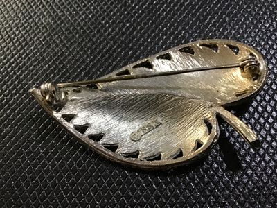 Sale Photo Thumbnail #95: A vintage gold-tone leaf brooch by BSK featuring a textured brushed metal finish, curved stem detail, and a rope twist border. The back is stamped '©BSK' and includes a standard pin stem with a rollover safety clasp. Shows light vintage wear consistent w