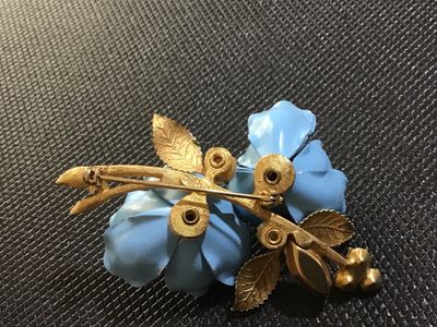 Sale Photo Thumbnail #85: A vintage Weiss gold-tone floral brooch featuring two light blue enameled flowers with blue rhinestone centers, faux pearl accents, a navette aurora borealis rhinestone, and green enamel leaves. Marked '© WEISS' on the back frame. Pin mechanism is intact