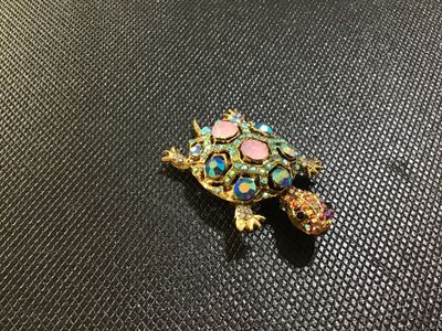 Sale Photo Thumbnail #68: Ornate gold-tone turtle brooch embellished with colorful rhinestones, including iridescent aurora borealis, blue, pink, and small accent stones. Features a filigree textured back with a standard pin stem and rollover clasp. In good vintage condition with 