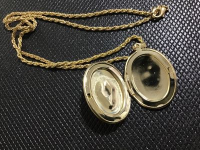 Sale Photo Thumbnail #111: Vintage oval gold-tone locket pendant featuring a central light pink porcelain-style rose detail surrounded by pink rhinestone accents. Suspended on a gold-tone rope chain with a lobster claw clasp. Opens to hold two photos or small mementos. Locket shows