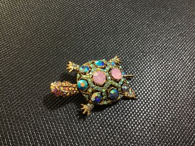 Sale Photo Thumbnail #67: Ornate gold-tone turtle brooch embellished with colorful rhinestones, including iridescent aurora borealis, blue, pink, and small accent stones. Features a filigree textured back with a standard pin stem and rollover clasp. In good vintage condition with 
