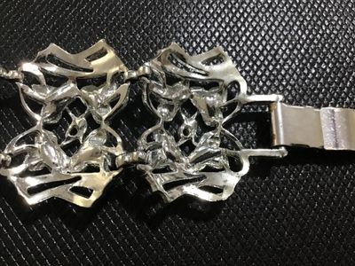 Sale Photo Thumbnail #107: A vintage silver-tone wide link bracelet featuring stylized floral textured leaf motifs within openwork geometric frames. Secured with a fold-over clasp. Appears to be mid-20th century costume jewelry in good condition with minor surface wear visible on t