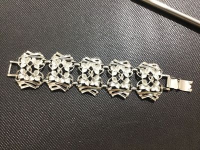 Sale Photo Thumbnail #104: A vintage silver-tone wide link bracelet featuring stylized floral textured leaf motifs within openwork geometric frames. Secured with a fold-over clasp. Appears to be mid-20th century costume jewelry in good condition with minor surface wear visible on t