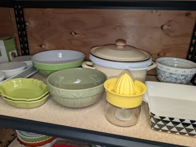 Sale Photo Thumbnail #20: Collection of ceramic kitchenware including green serving bowls, a covered casserole dish, a yellow manual citrus juicer, and a patterned baking dish.