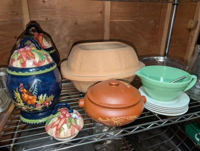Sale Photo Thumbnail #17: Collection of kitchenware featuring a terracotta Schlemmertopf baker, a green jadeite-style batter bowl, a small reddish clay pot, and ceramic canisters with rooster and vegetable motifs.