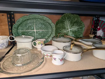 Sale Photo Thumbnail #18: kitchenware including green Bordallo Pinheiro cabbage leaf platters, white ceramic saucepans with glass lids, small porcelain creamers, and clear pressed glass dishware.