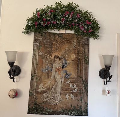 Sale Photo Thumbnail #18: Woven tapestry wall hanging featuring an angel design by Lena Liu, topped with a faux greenery floral arch and flanked by a pair of metal wall sconces.