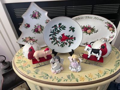 Sale Photo Thumbnail #15: Collection of holiday decor including floral porcelain trays, a cardinal decorative plate, bird ornaments, angel figurines, and farm animal sled accents.