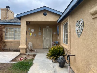 Sale Photo Thumbnail #29: Exterior view of a stucco single-family house featuring an entryway decorated with wall art, a heart-shaped metal sign, and potted plants.