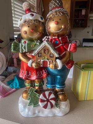 Sale Photo Thumbnail #25: Large decorative gingerbread couple Christmas statue holding a gingerbread house, featuring glossy painted finishes, embedded faux jewels, and winter accents.