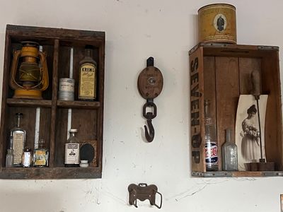 Sale Photo Thumbnail #19: Rustic wall-mounted wooden crates displaying vintage collectibles, including a Kreml Hair Tonic bottle, a yellow lantern, a vintage Pepsi-Cola bottle, and a Prince Albert tobacco tin, alongside an antique wooden pulley.