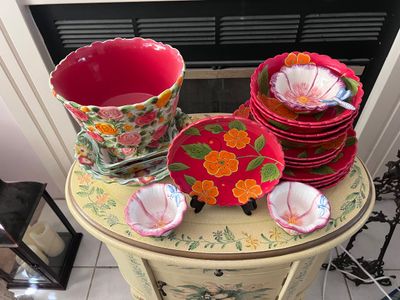 Sale Photo Thumbnail #9: Collection of hand-painted floral ceramic tableware, including a large scalloped planter, stacked plates, and small flower-shaped bowls displayed on a painted accent table.