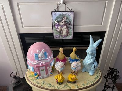 Sale Photo Thumbnail #11: Collection of Easter decorations featuring an illuminated pink egg house, duck figurines in tutus, a light blue ceramic bunny, textured chick figurines, and a hanging metal sign.